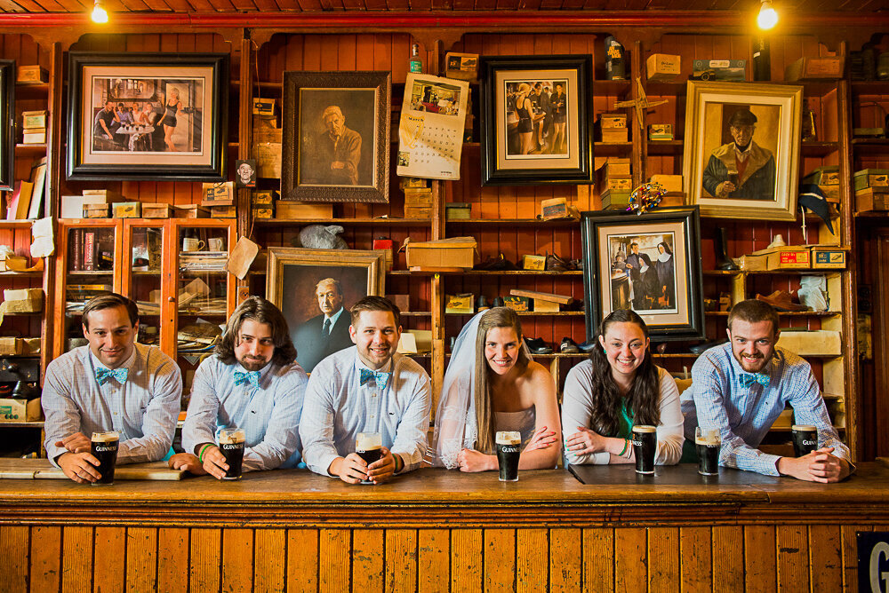 Bride with groom and groomsmen in traditional Irish pub in Dingle wearing baby blue bow ties and drinking Guinness