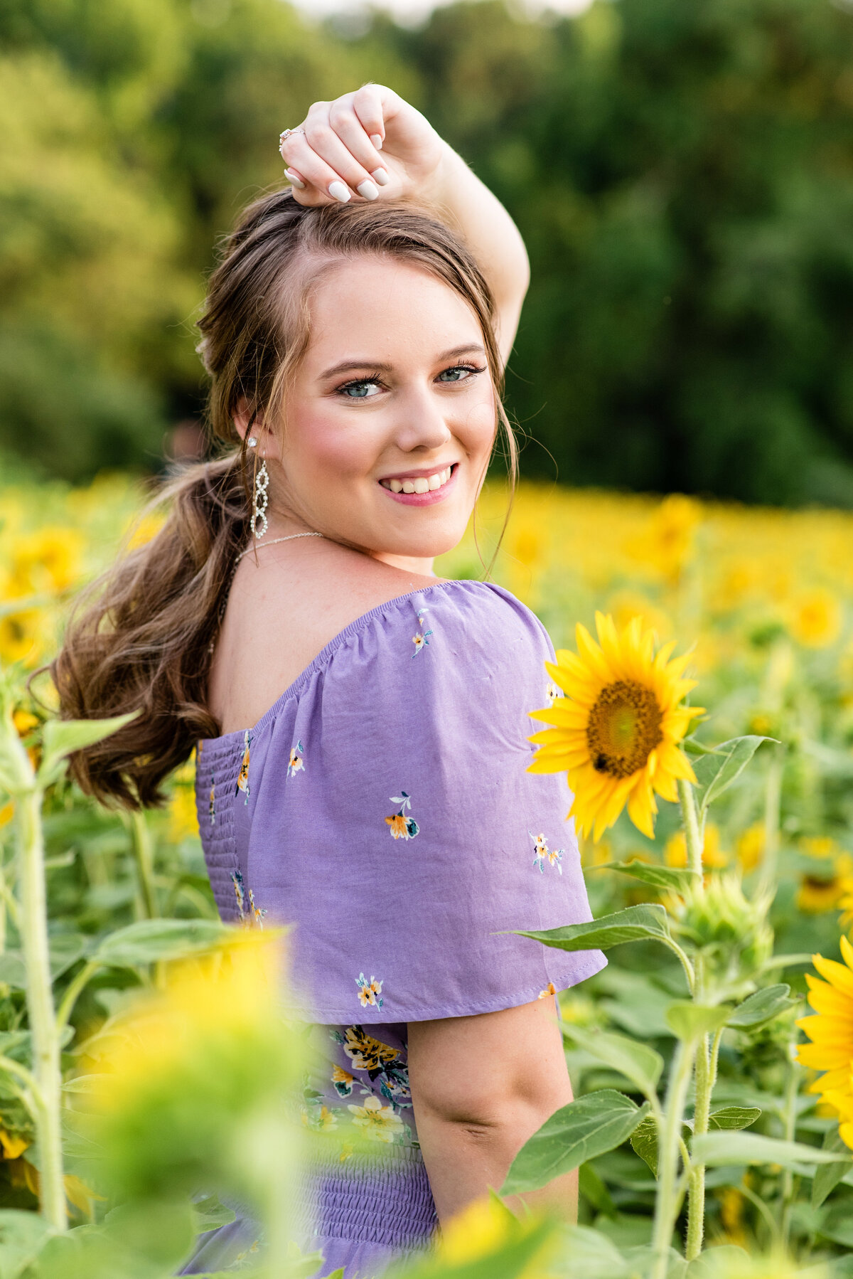 Midlothian high school senior girl wearing a purple jumpsuit poses for her senior pictures in a sunflower field.
