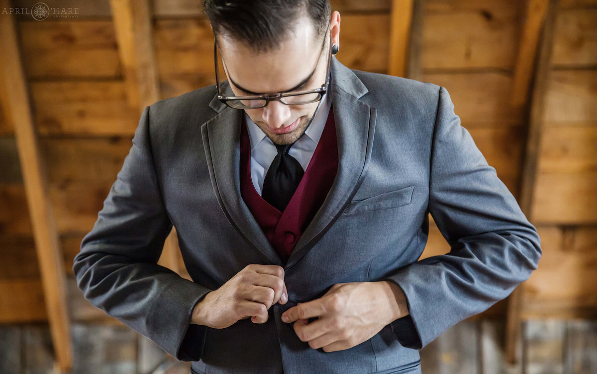 Groom buttons his suit jacket before wedding ceremony at The Barn at Evergreen Memorial Park in Colorado