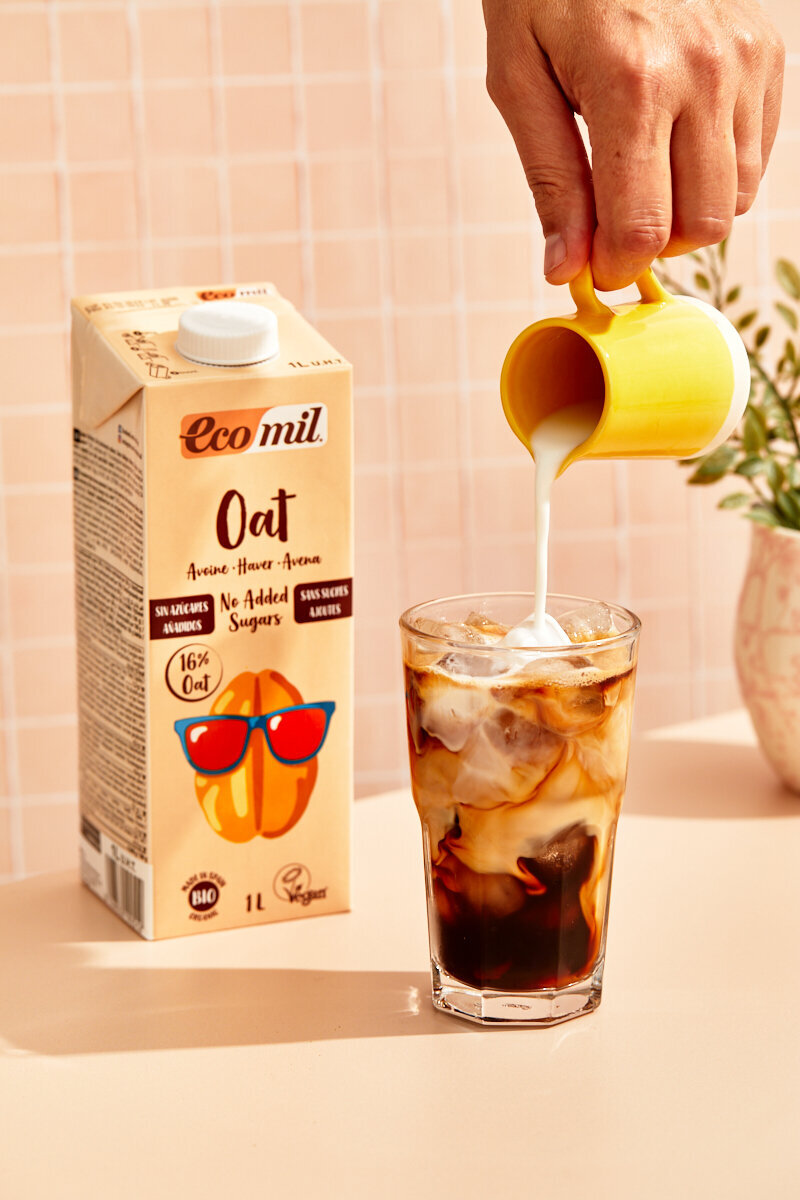 Hand pouring Ecomil nut milk into a tall class of cold brewed coffee.
