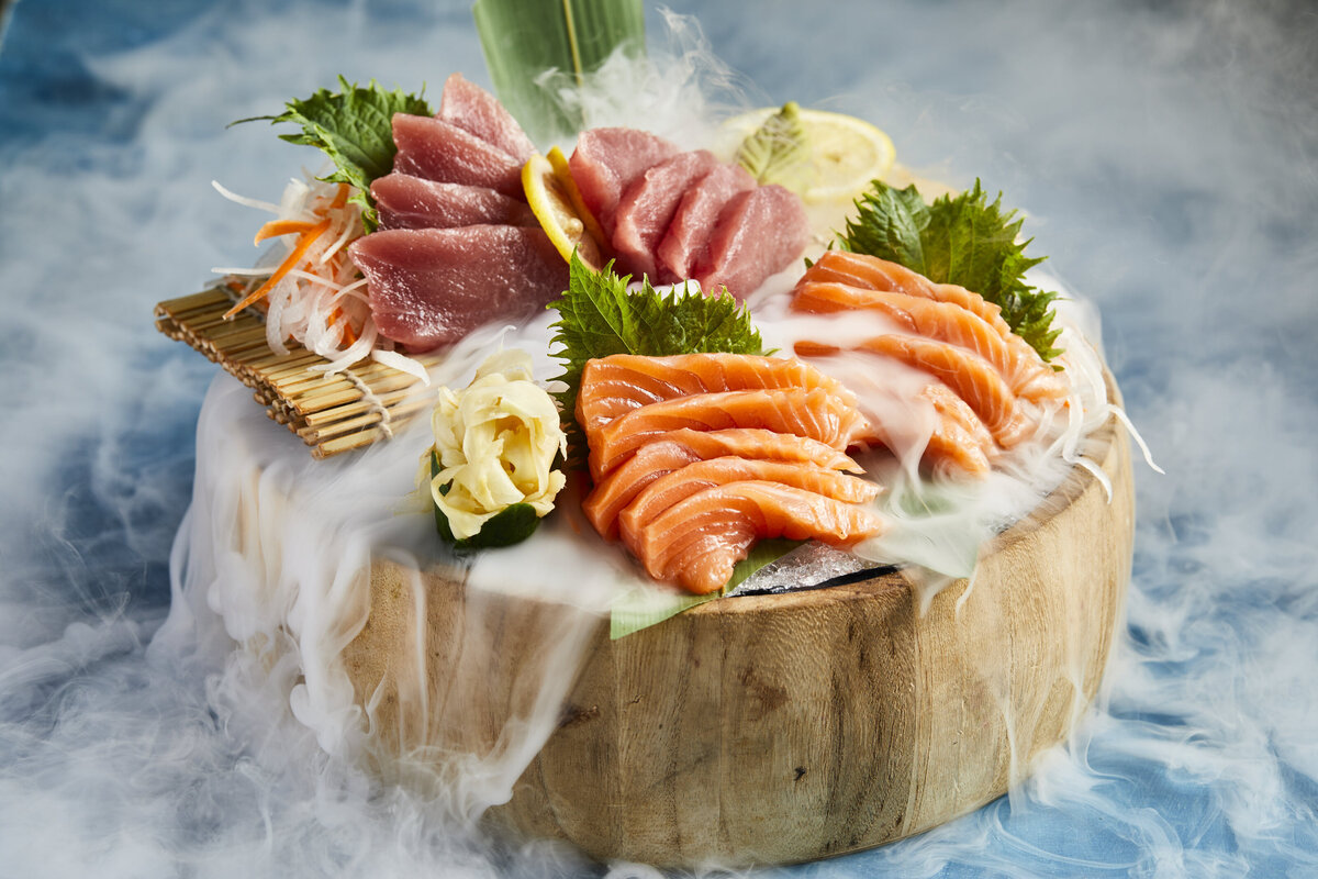 Circular wood block with sliced raw fish on top and smoke coming out from the underneath.