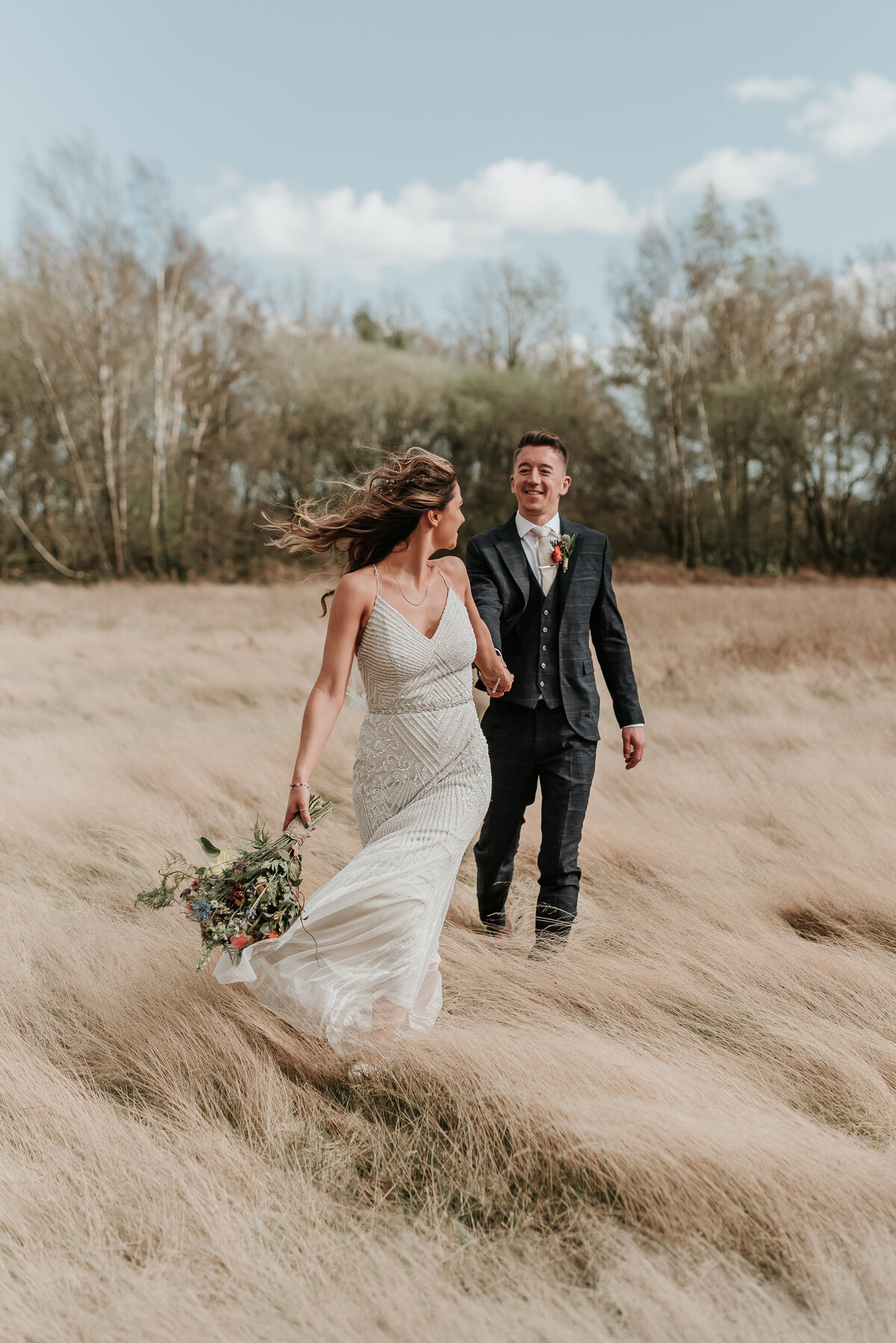 Bride leads Groom through a long grass field at Two Woods Estate