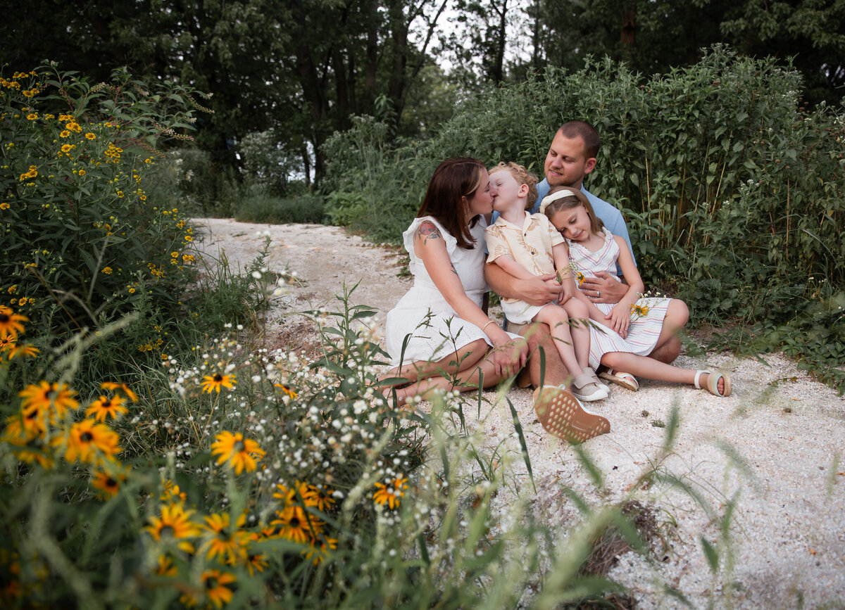 Mommy kisses her child during their summer photos in Havre de Grace, Maryland. The other family members cuddle and relax around them.