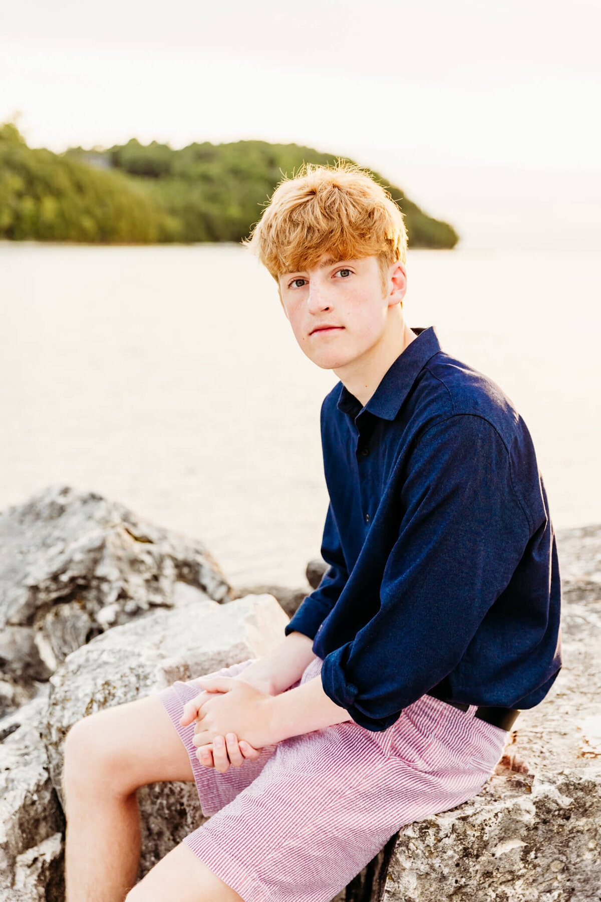 young man sitting on rocks rubbing hands together by senior photographer Ashley Kalbus