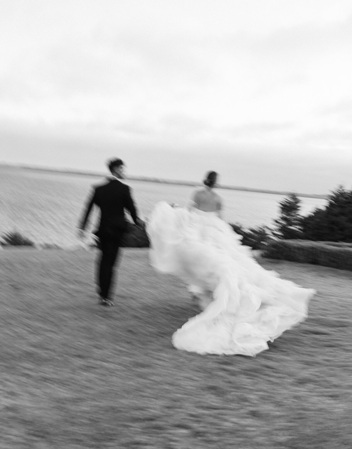 Bride and groom running in field.