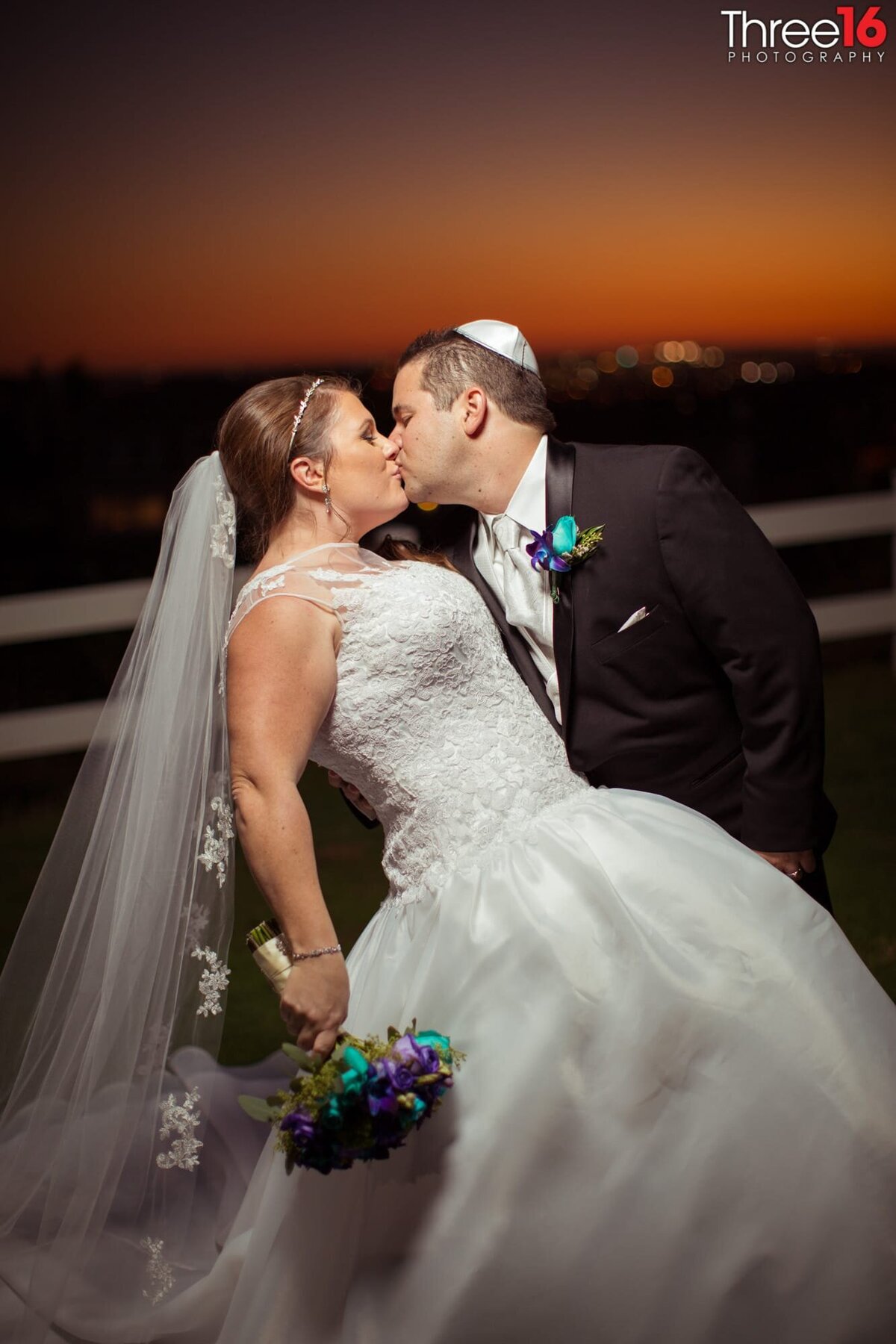 Groom dips and kisses his Bride during photo shoot just as the sun is setting