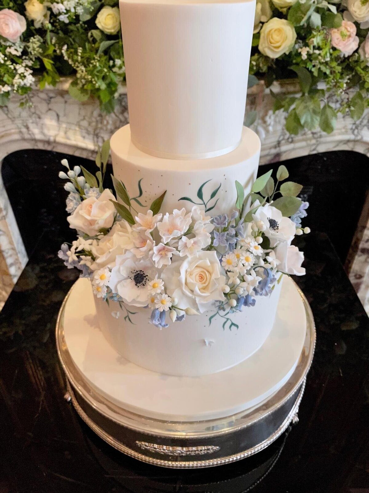 A two tier wedding cake with lots of sugar flowers covering the second tier