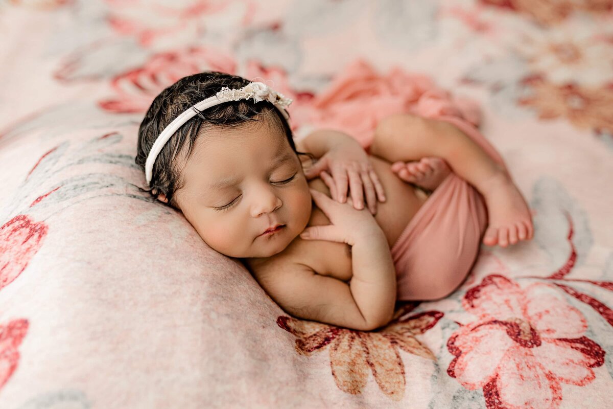 charlotte newborn is wrapped in a pink sheer wrap wearing a pink bow and laying on a floral drop