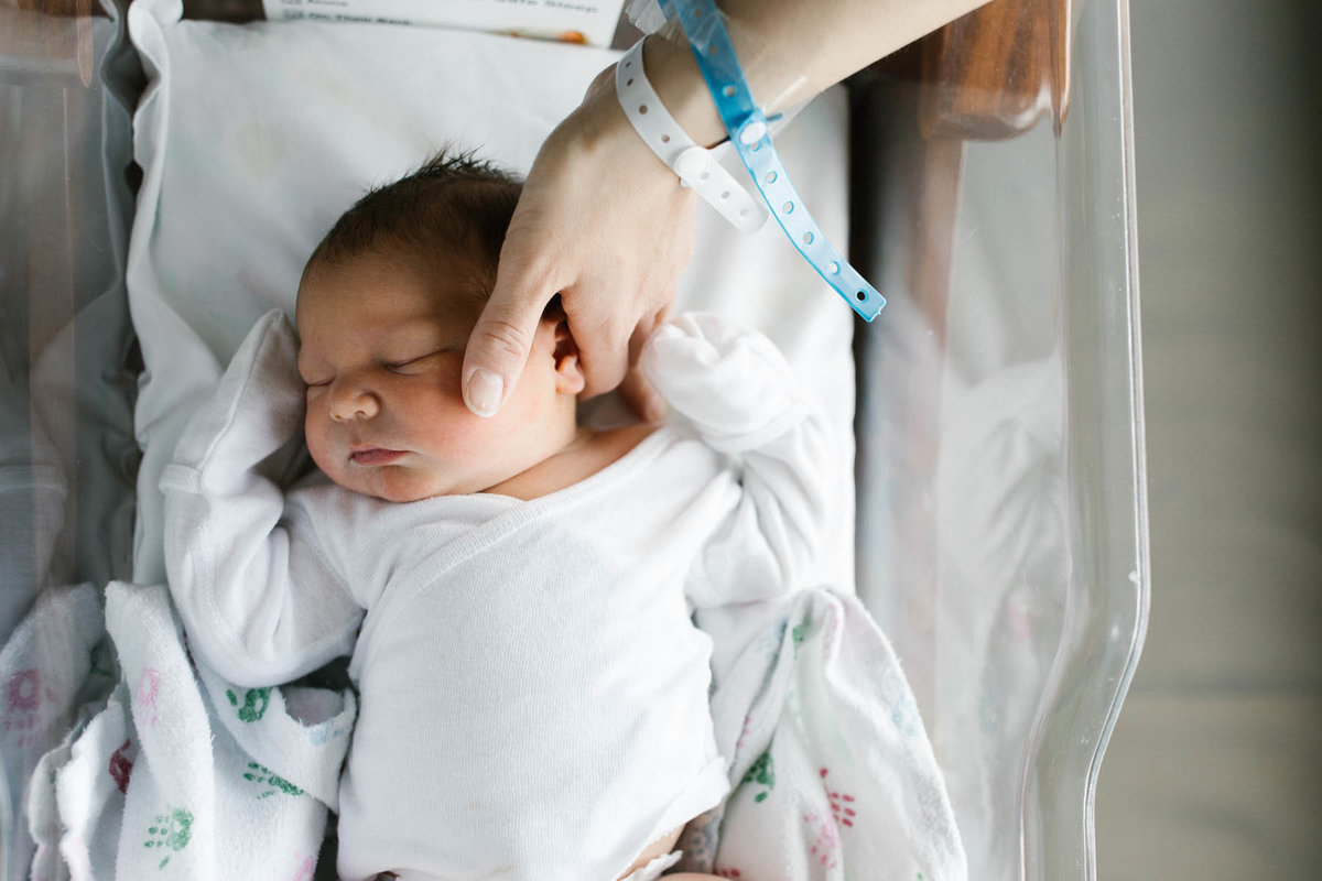 Mother touches 48 hour old newborn baby boy in hospital bassinet by Elle Baker Photography