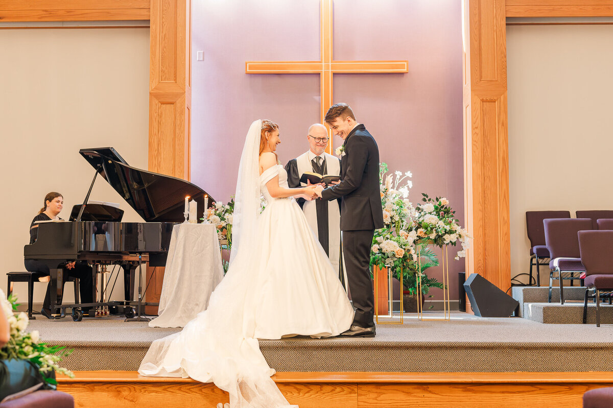 A bride and groom laughing while they exchange vows in their church in Cary on their wedding day while enjoying their Raleigh wedding photography session by JoLynn Photography