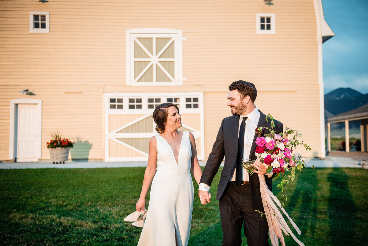 Couple holding hands and laughing together with a yellow barn behind them