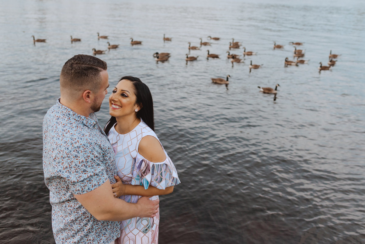 engaged couple standing by the water's edge with canada geese in the water