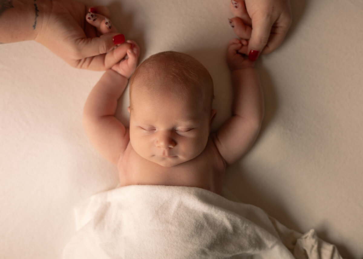 Maddie Rae Photography top angle of baby sleeping with his arms up. mom is holding his hands