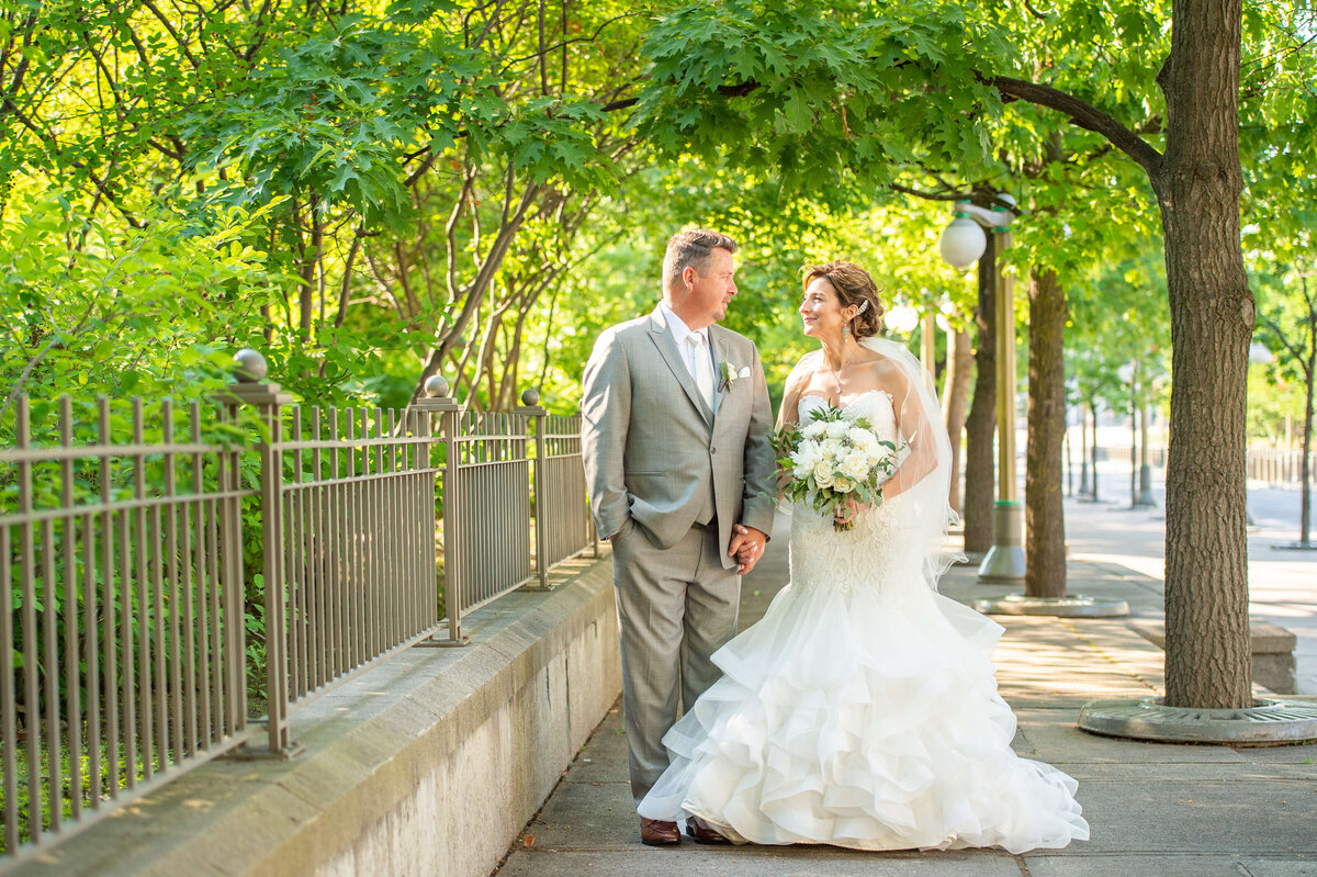 bride and groom walking hand-in-hand on their wedding day in Major's Hill Park as part of their Chateau Laurier wedding.  Captured by Ottawa wedding photographer JEMMAN Photography