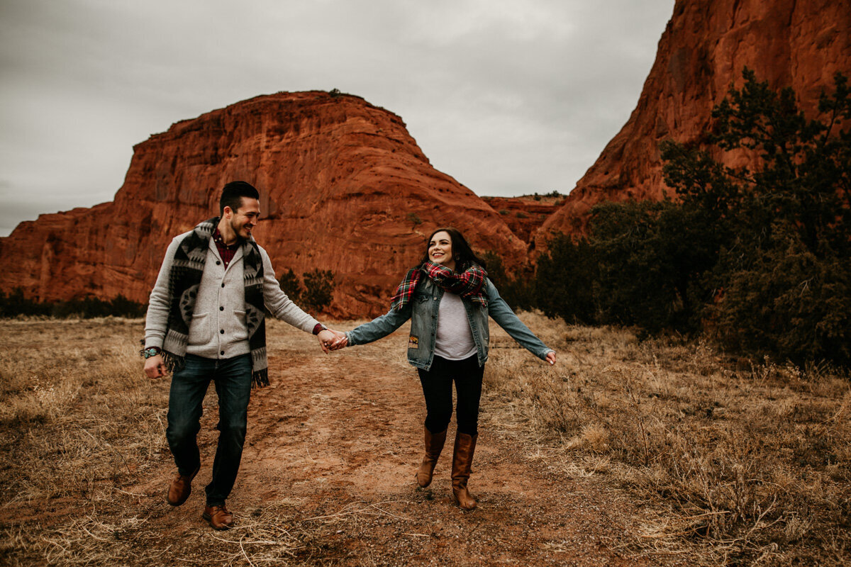 engaged couple running in front of a red rock mountain
