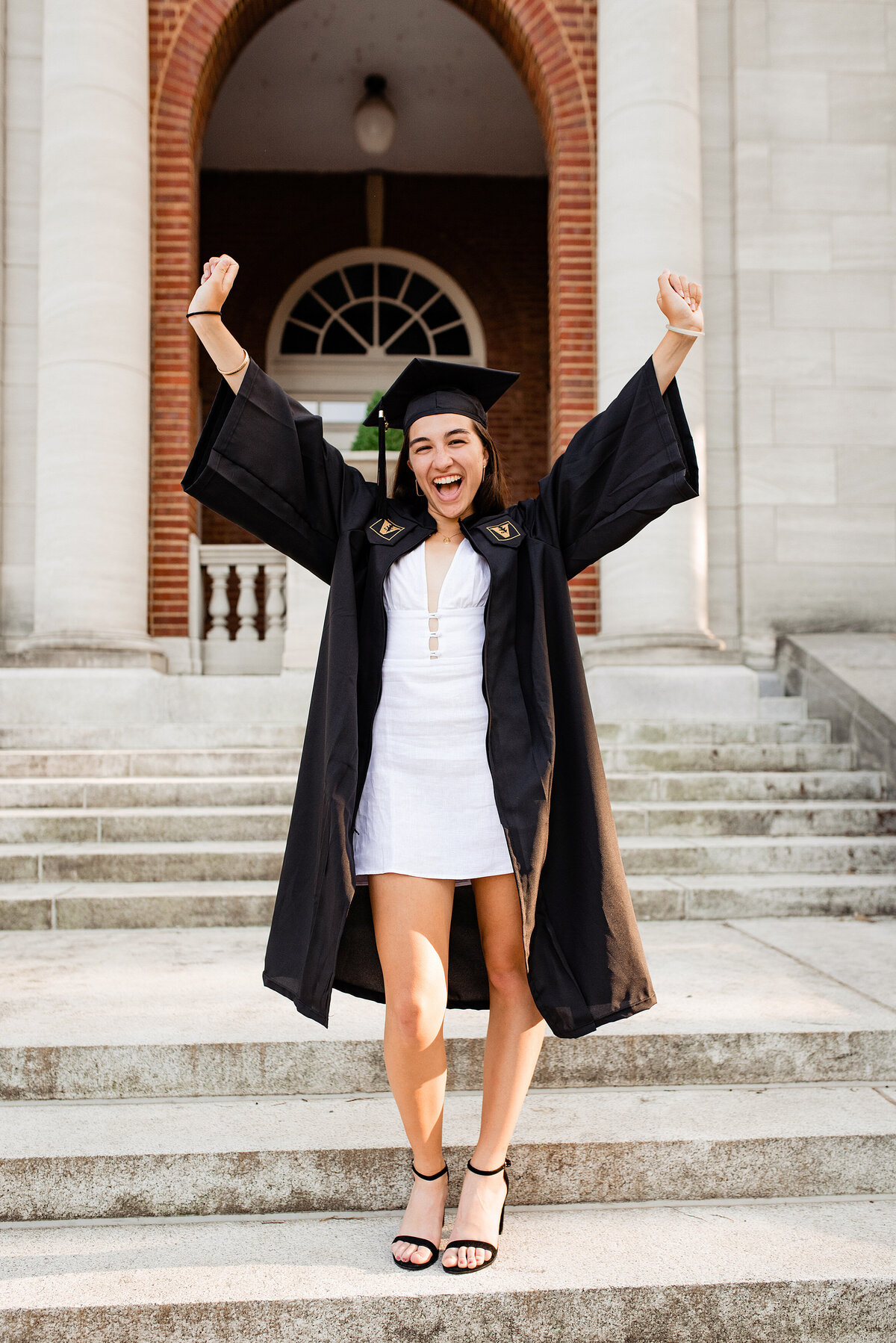 Vanderbilt senior wearing cap and gown celebrating with arms in the air