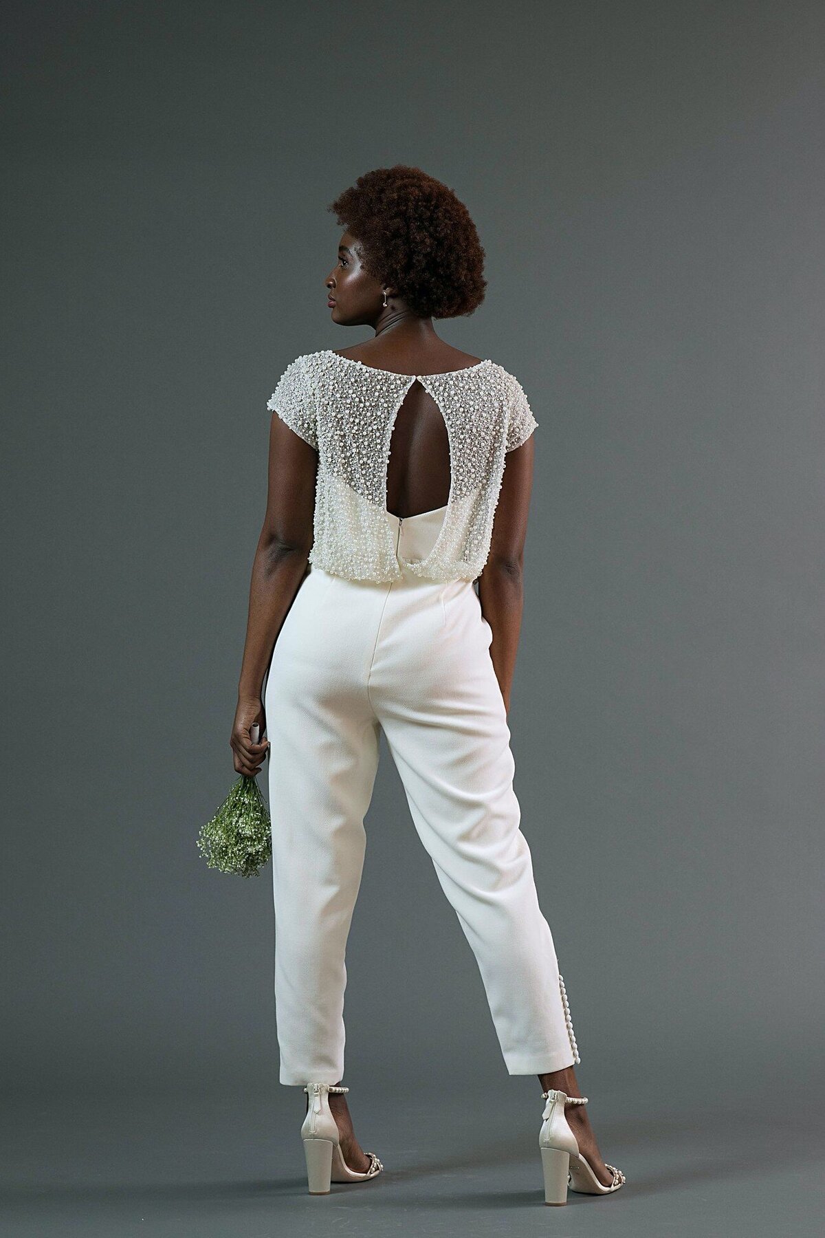 The Jonah bridal jumpsuit is a wool crepe foundation with a strapless bodice and cropped pants. The bloused pearl topper features a keyhole back.