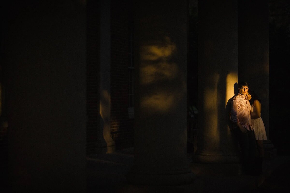 A couple stands in a dramatic columned hallway, illuminated by a warm, golden light that highlights their silhouette