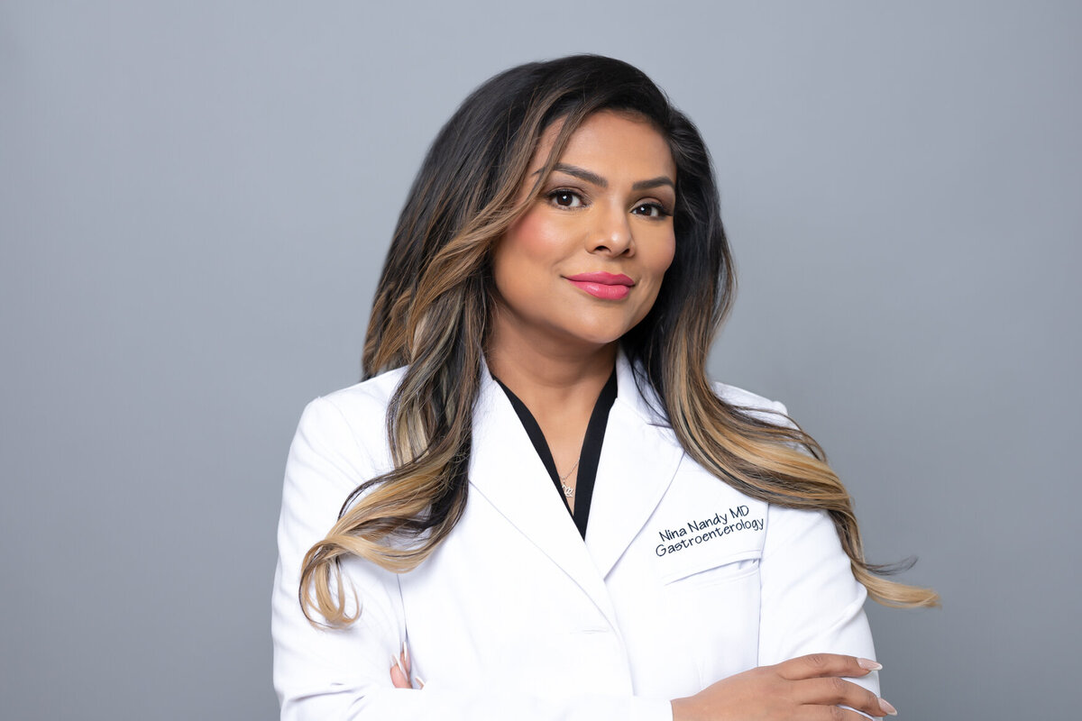 a headshot of a doctor woman wearing a white coat looking straight to the camera with a smile