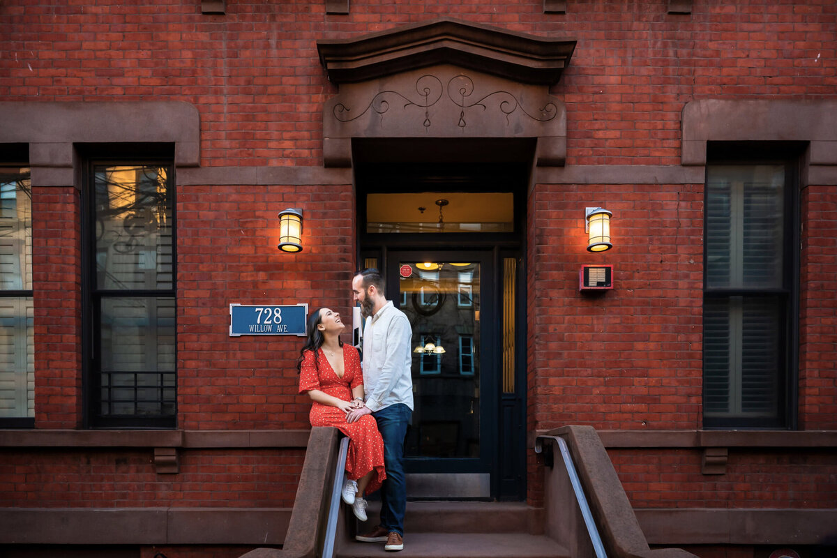 Woman wearing a red dress and man wearing a white shirt standing on the stoop of their Hoboken, New Jersey apartment