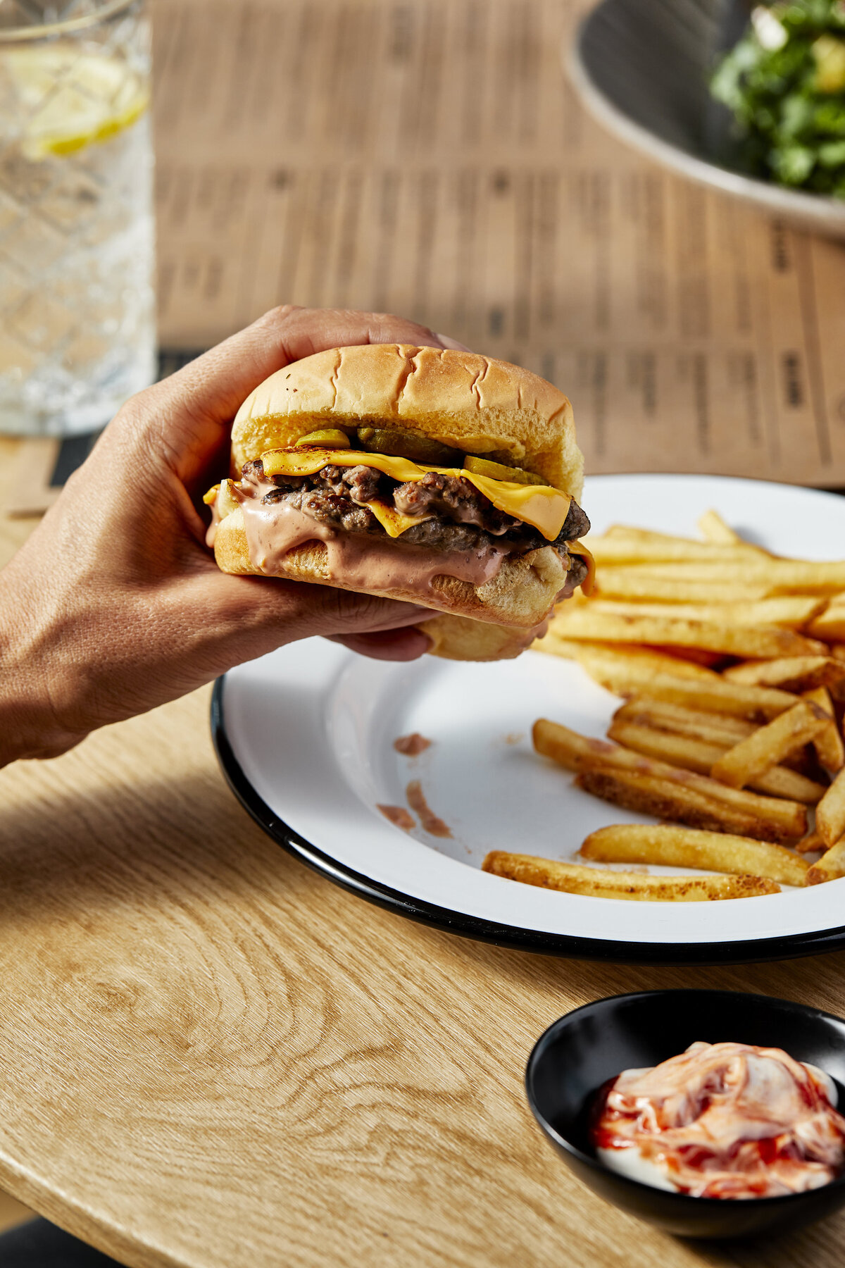 A hand holding a sandwich over a plate of fries.
