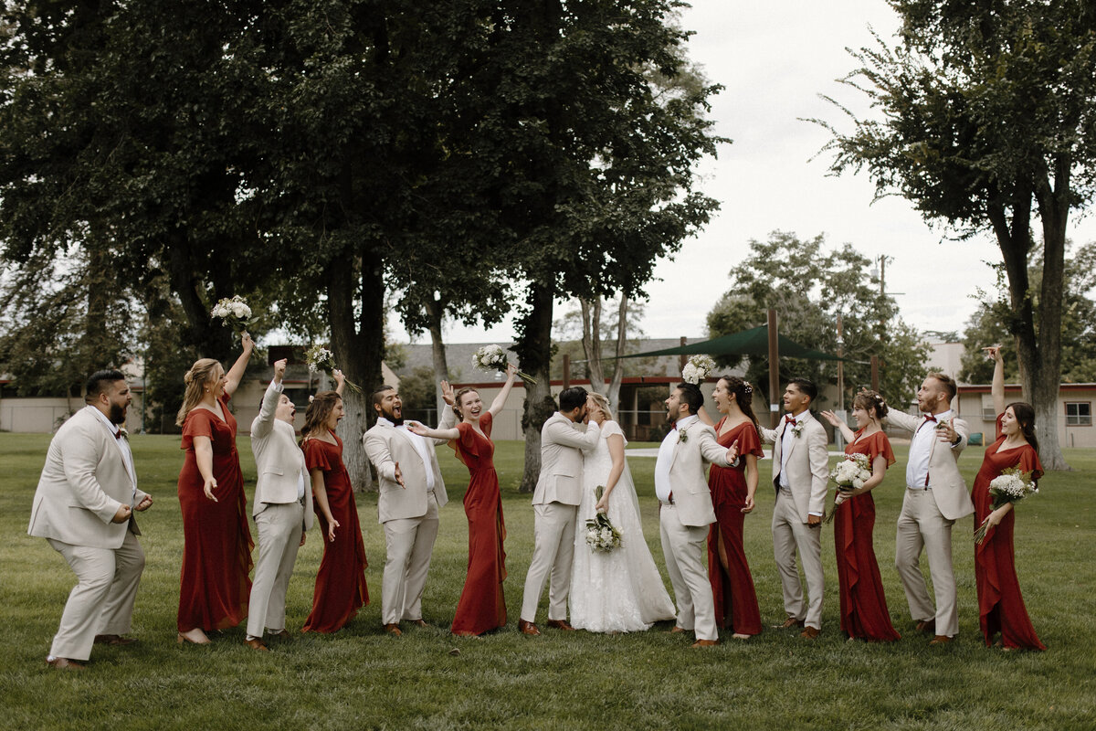 bridesmaids and groomsmen celebrating as bride and groom kiss