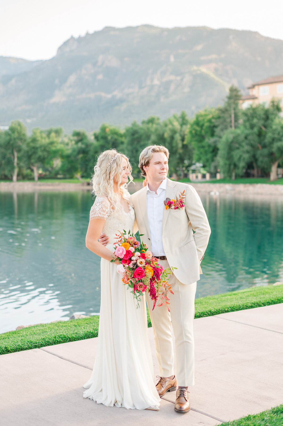 Blonde couple standing on a path by a lake on their wedding day at the Broadmoor Hotel.