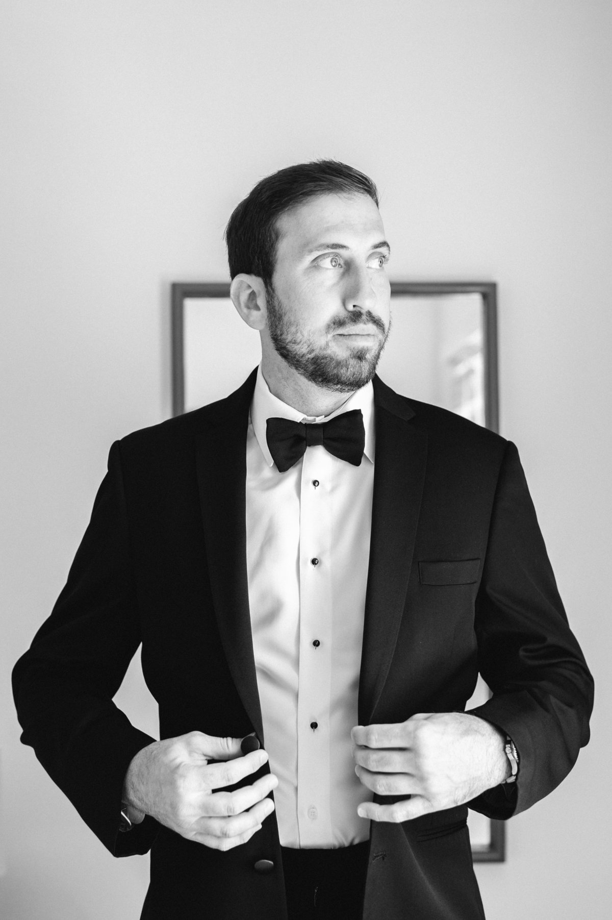 groom buttoning coat wearing black bow tie