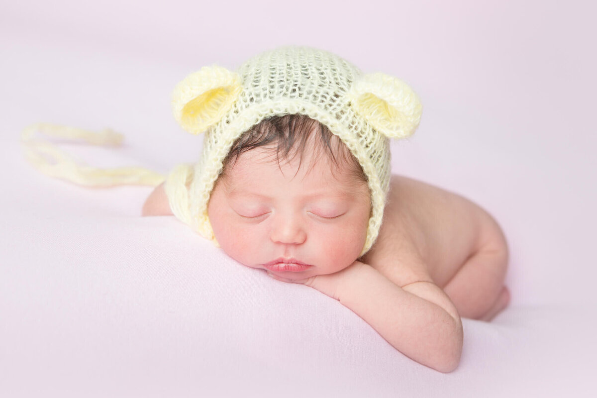 Baby girl asleep leading on her hands which wearing a little yellow bonnet taken by Los Angeles newborn photographer