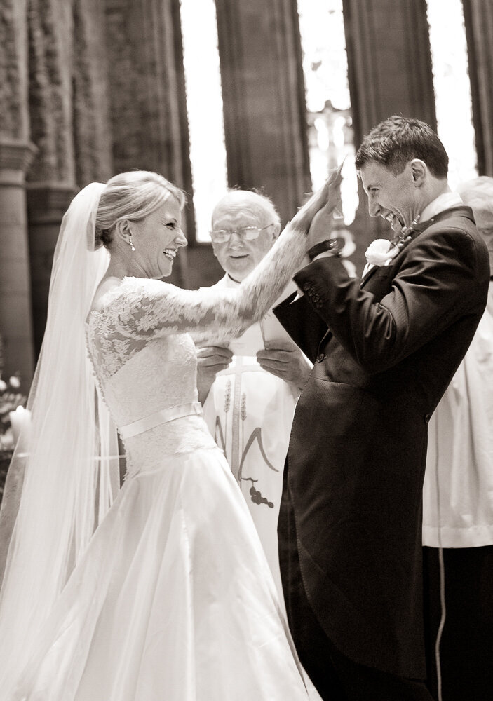 bride wearing a ballgown style dress with statement lace, long sleeves giving a high five to her groom after exchanging the rings in Killarney cathedral