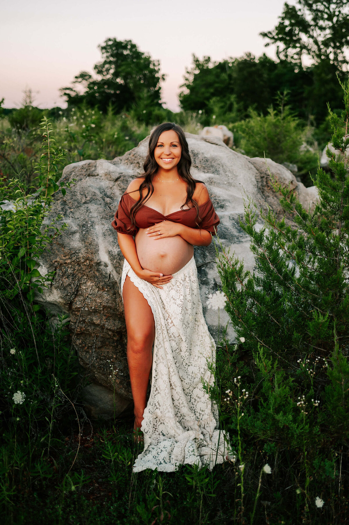 maternity photo of mom leaning against rock outdoors holding baby bump in Springfield MO