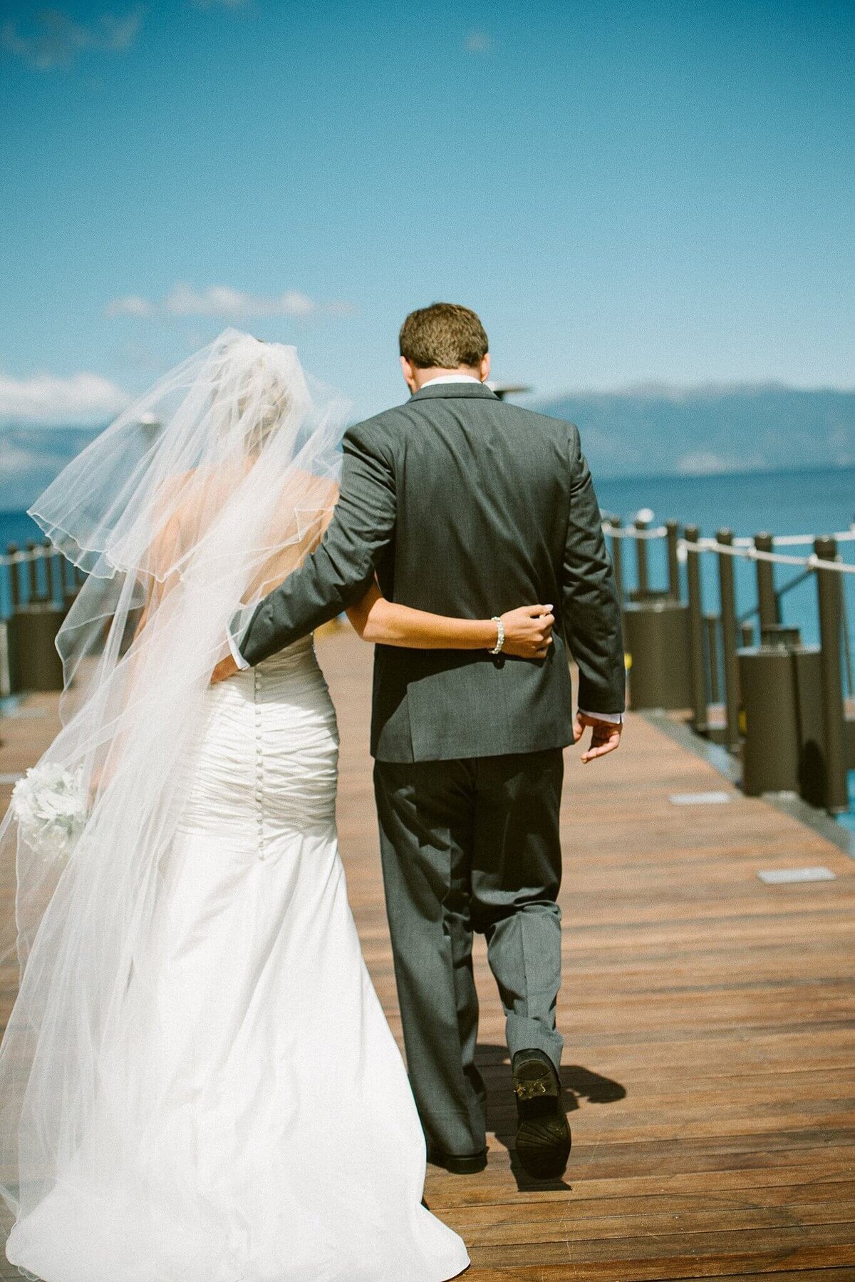 bride and groom walking towards end of pier at west shore cafe in lake tahoe