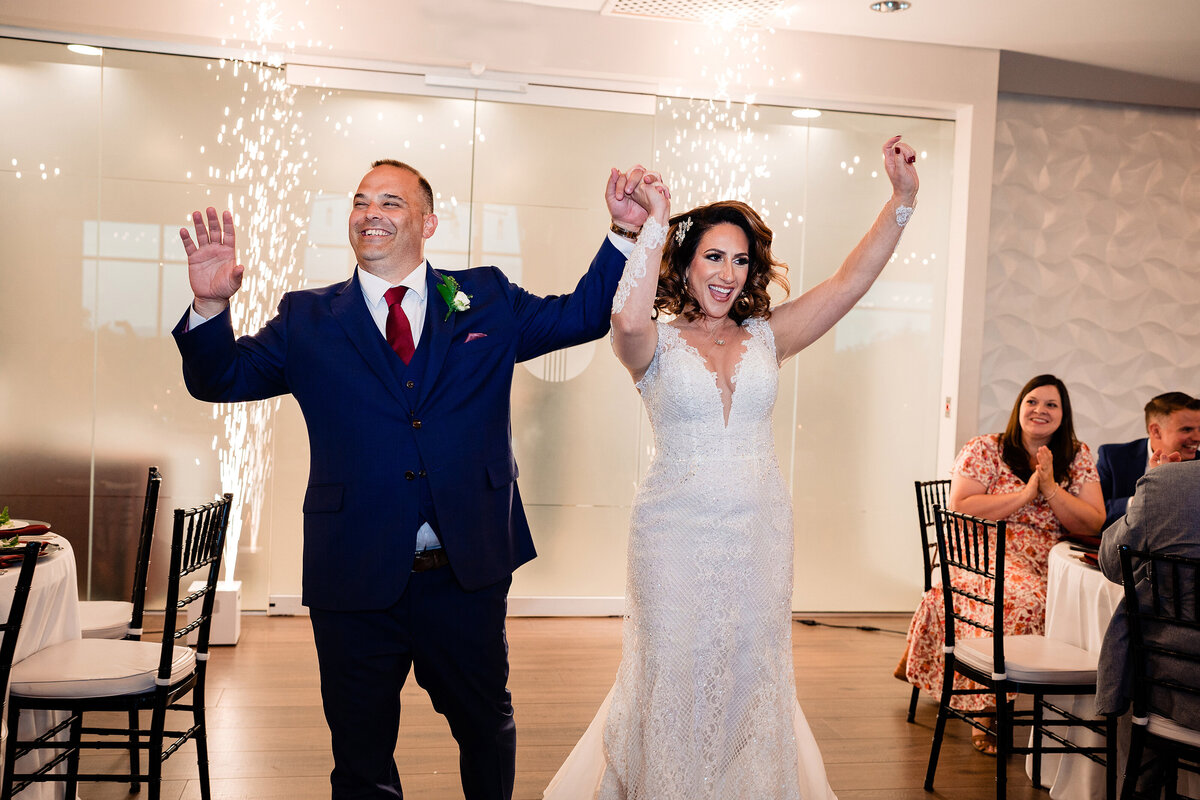 Newlywed couple jumping and dancing during their reception entrance with cold sparklers going off behind them