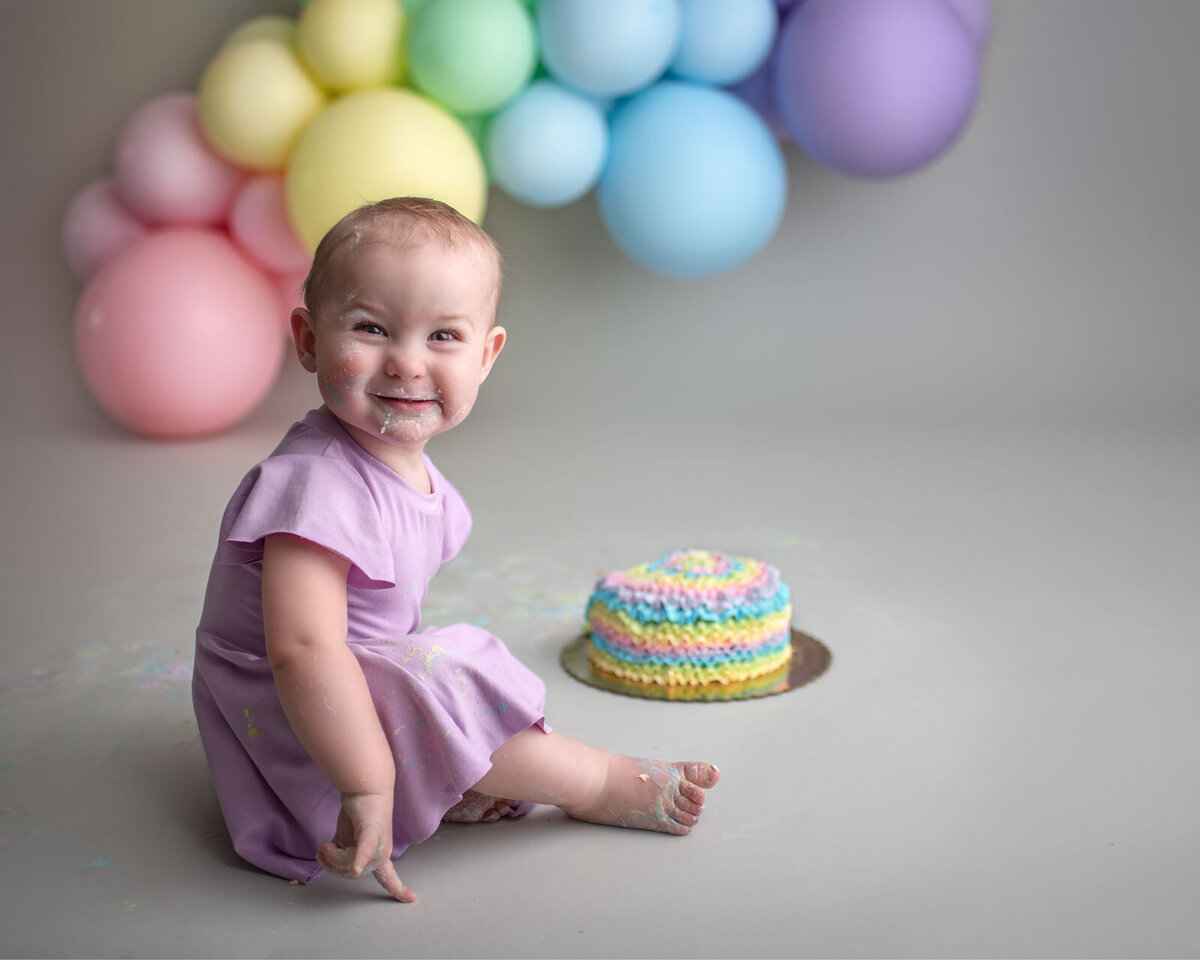 smiling baby eating a rainbow cake by st. louis cake smash photographer