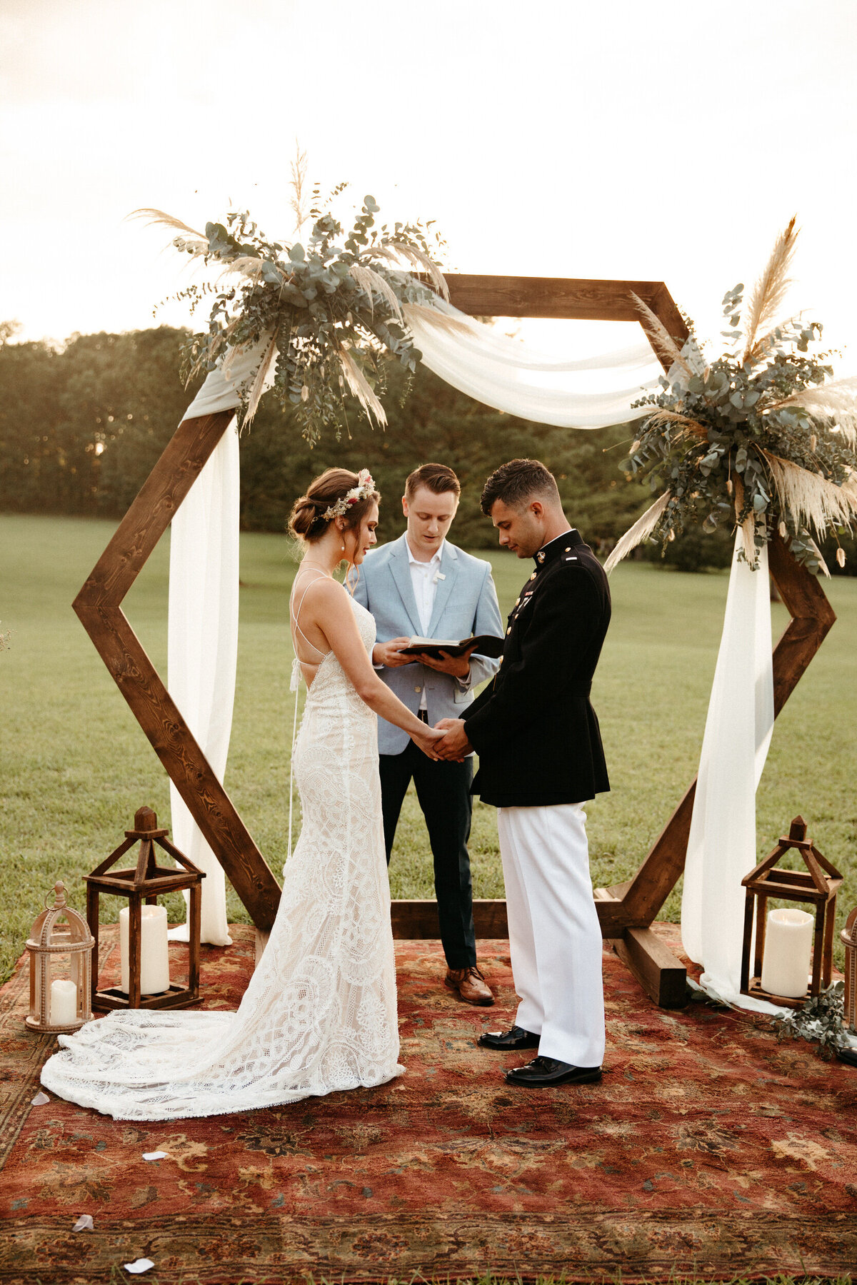 Boho wedding ceremony with hexagon arch, vintage rug, and candles inside lanterns