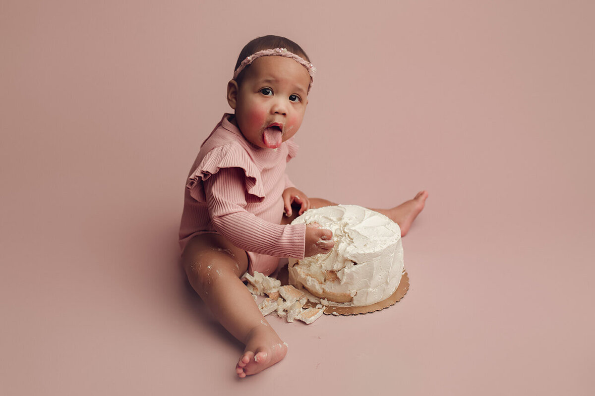 a one year old girl smashing a cake with her tongue out