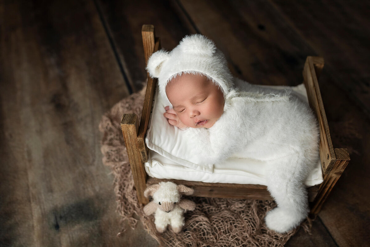 Baby boy posed on a newborn bed wearing a white bear outfit and bonnet.