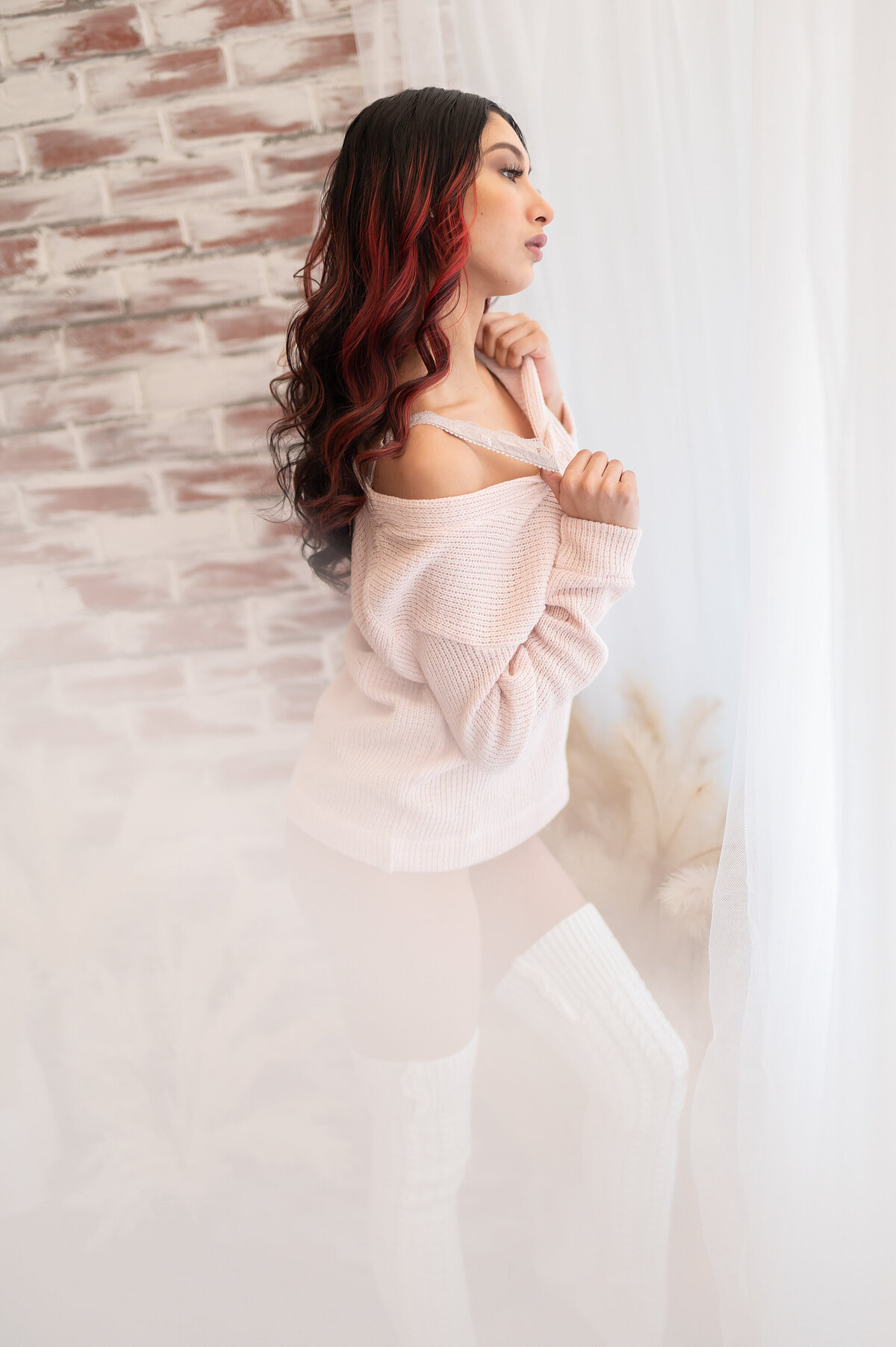 A brunette woman with magenta highlights poses in our Waukesha photo studio for a cozy studio boudoir session.