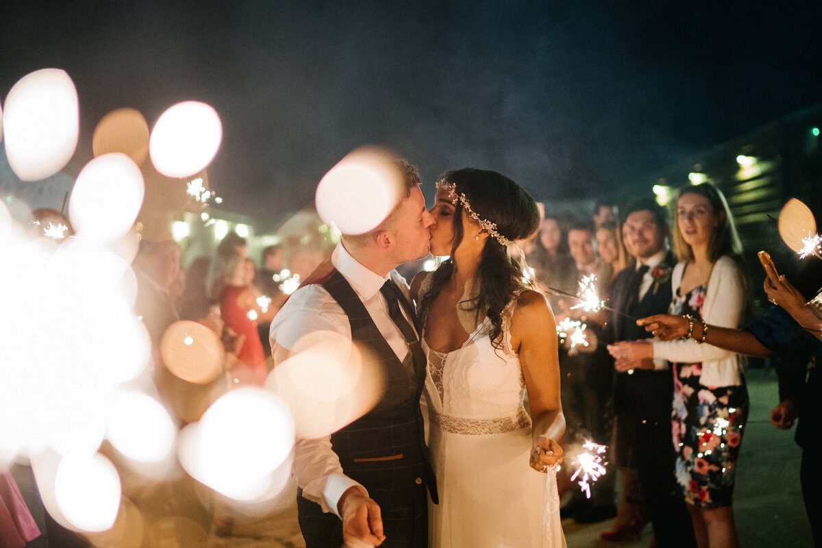 A wedding couple kissing during a sparkler exit