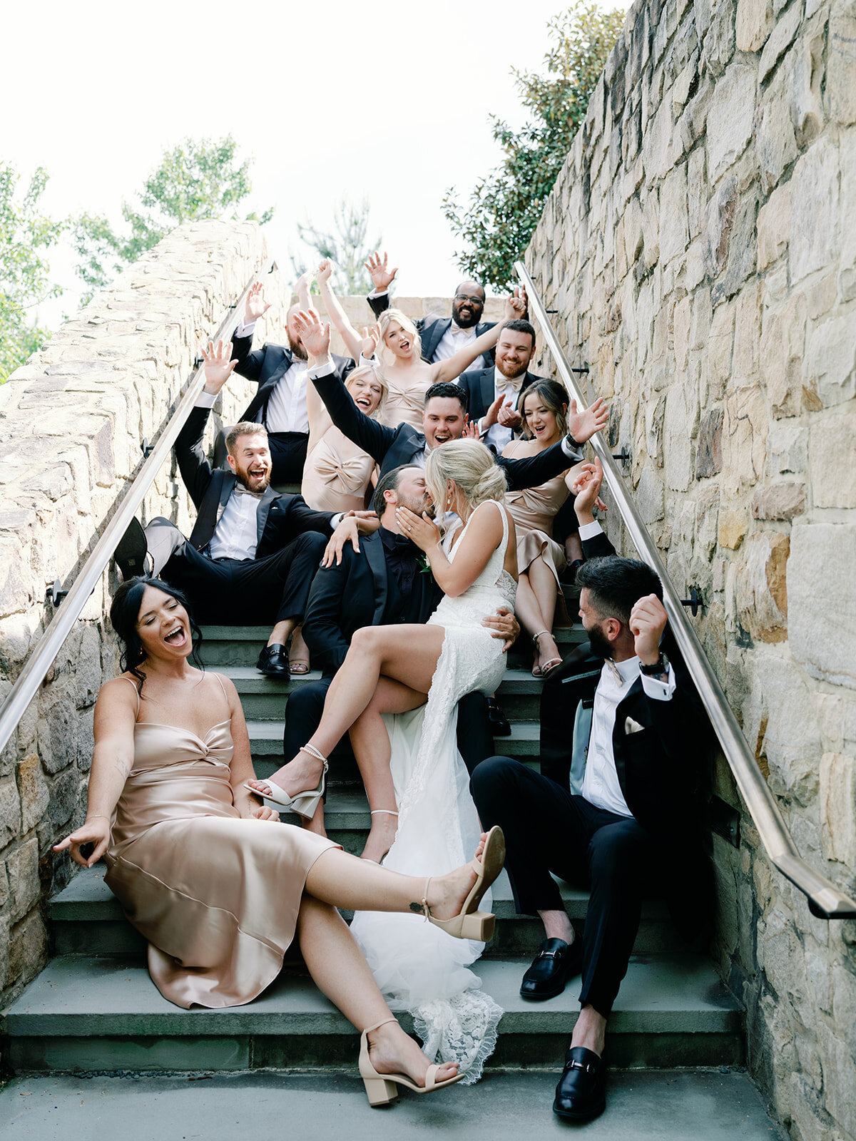 Bride and groom and their bridal party sit on the steps along the stone wall at salamander resort in middleburg, virginia.