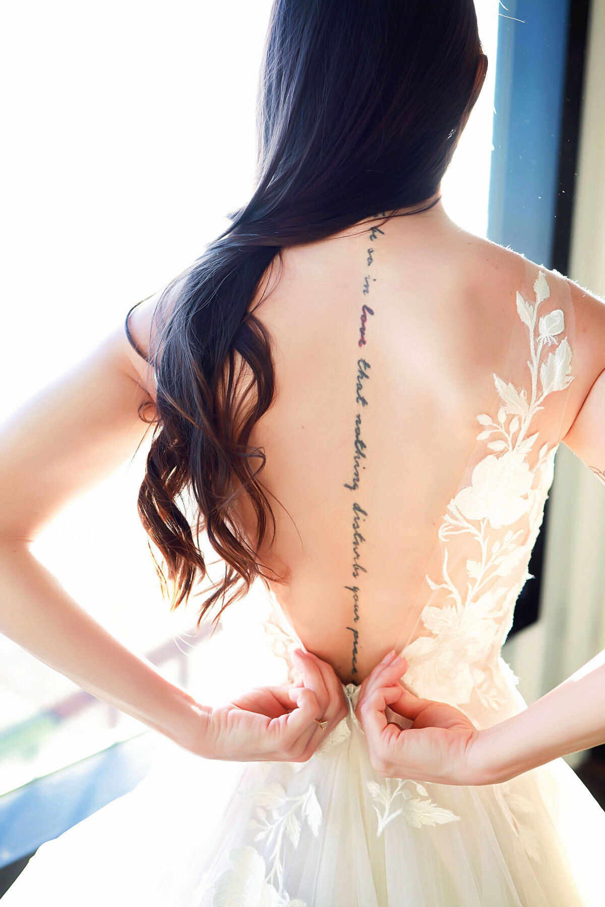 A bride buttoning her dress, with a beautiful back tattoo showing.