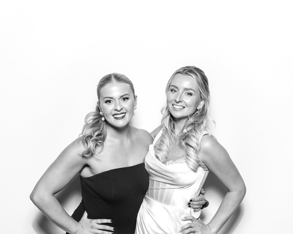 2 guests posing for a white backdrop with a kardashian glam photo booth with b&w prints for weddings, corporate events and other events
