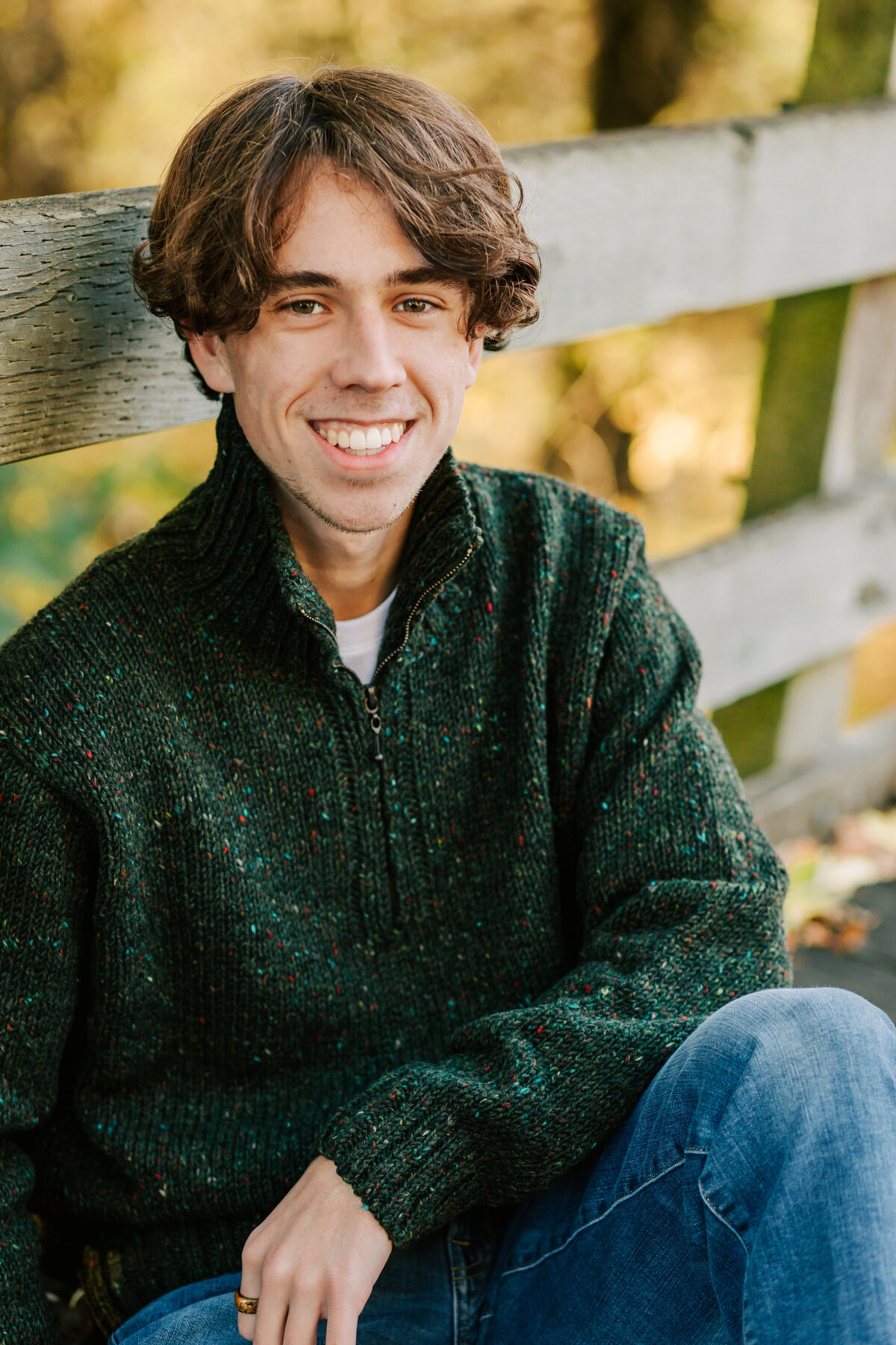 A young man in a green sweater sits against a fence