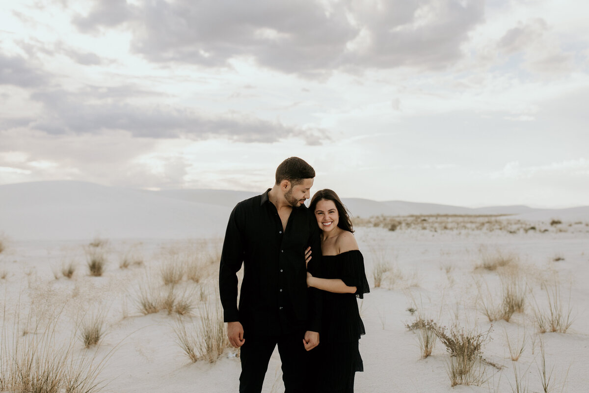 engaged couple standing together in the desert white sand dunes