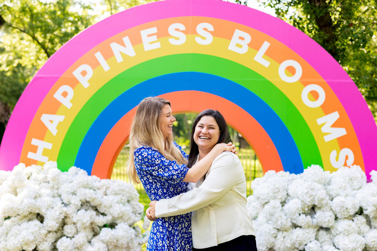 A couple hugging in front of a large rainbow cutout.