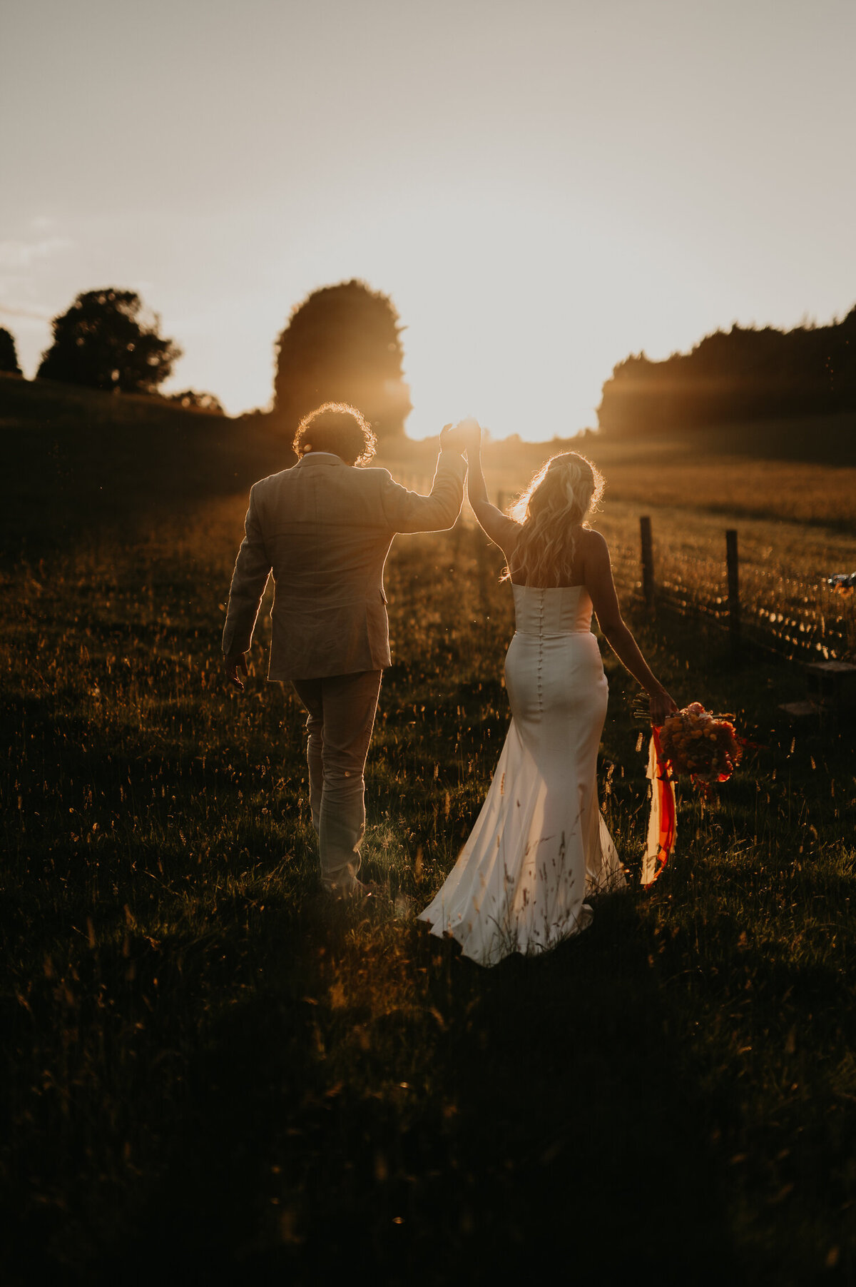 Bride and groom walk in a field during sunset at Hadsham Farm wedding venue in Banbury.