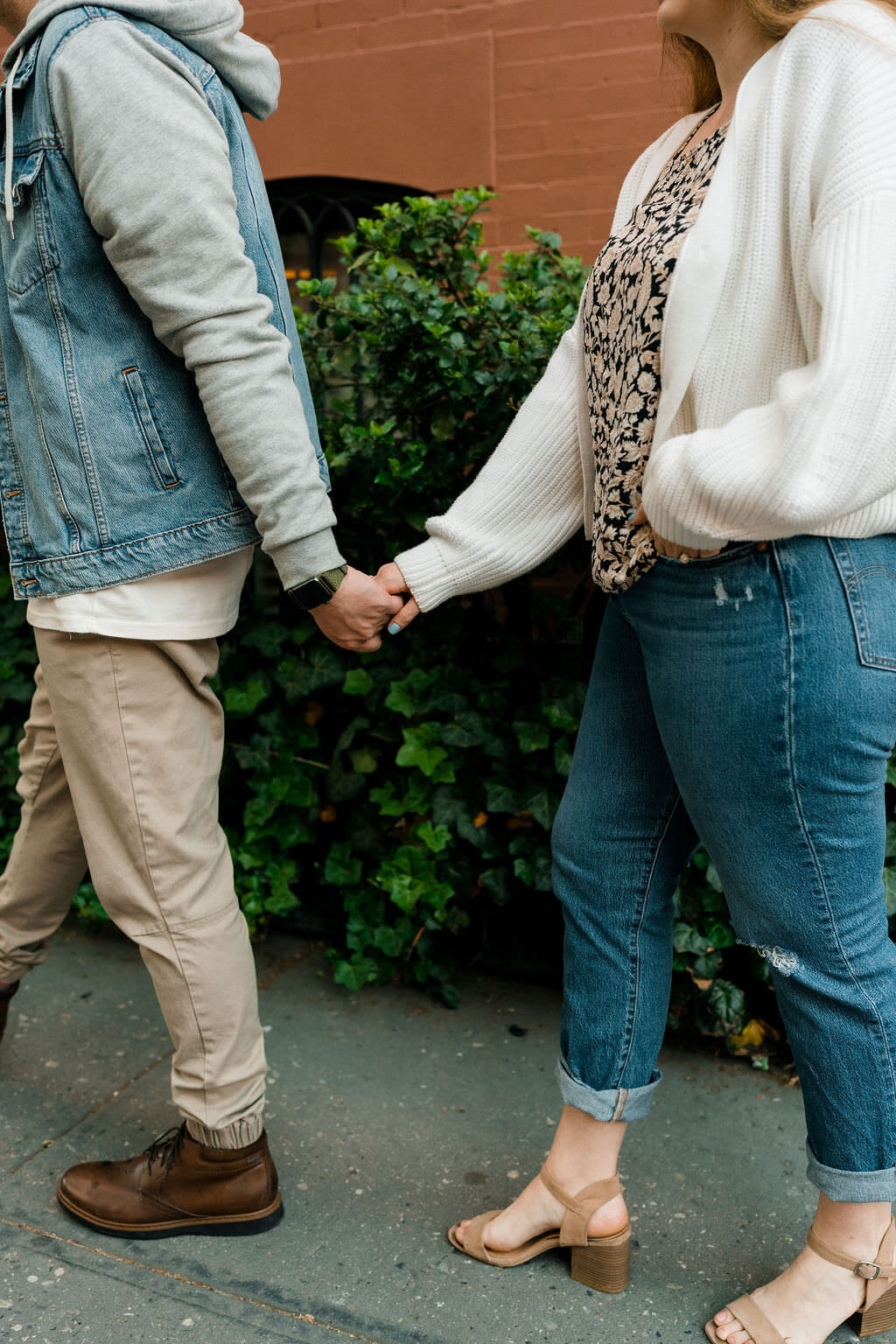 man reaching back and holding womans hands on a city sidewalk