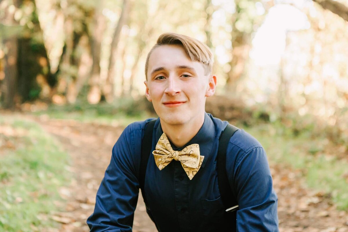 A teenage boy in blue shirt and gold bowtie looks at the camera smiling