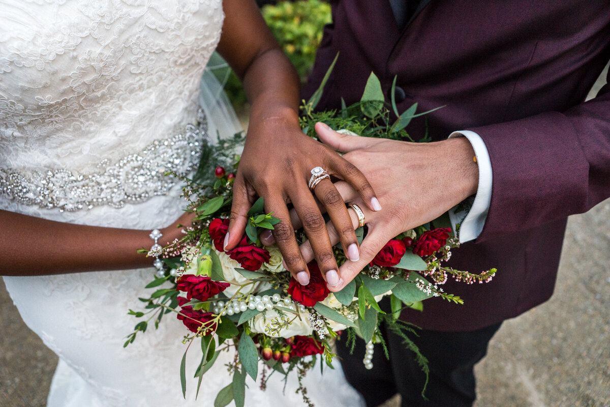 Bride and groom's hand holding floral bouquet showing the both wedding rings
