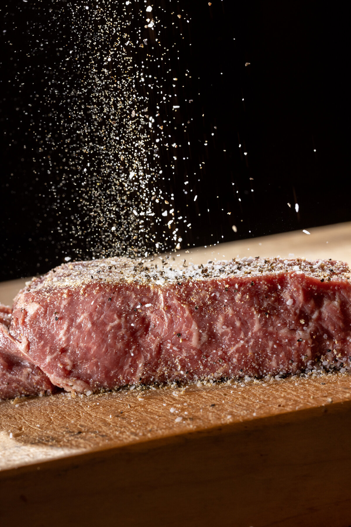 Seasoning being poured onto a steak